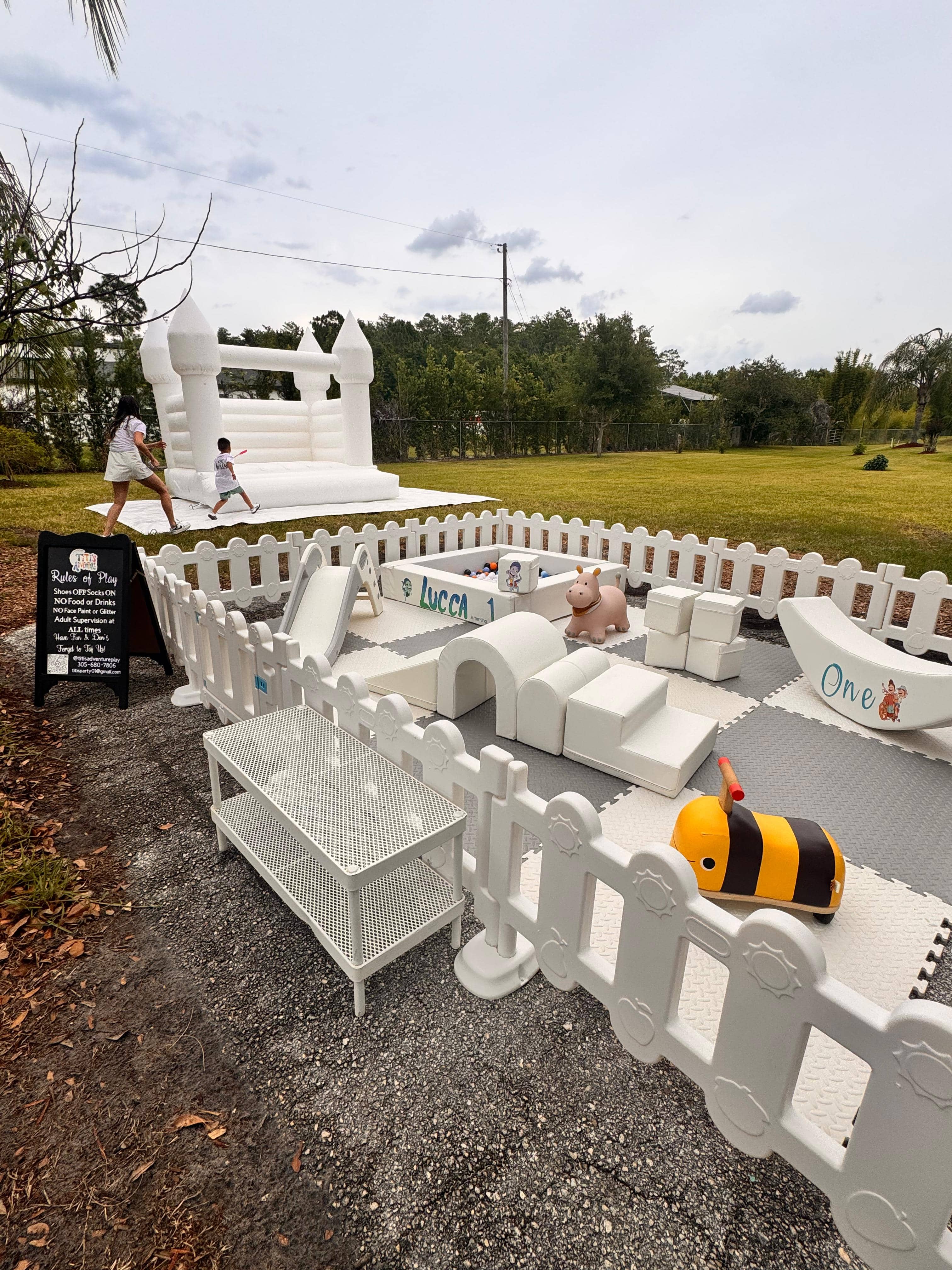 Little Adventurer Deluxe outdoor soft play setup — all-white fenced play area with white bounce house and colorful ball pit in a Florida backyard