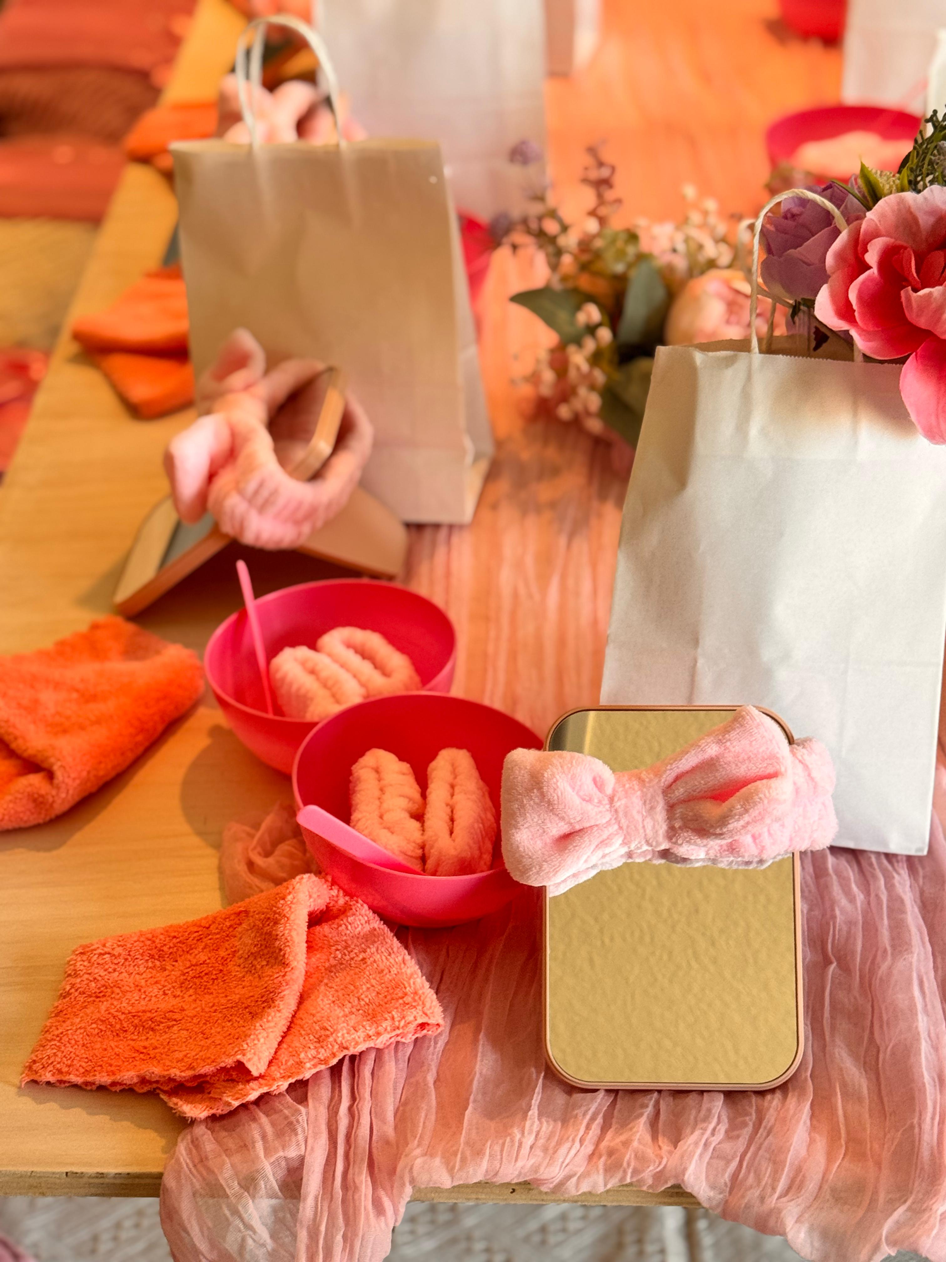 Styled Sparkle Spa party table close-up — spa headbands, orange towels, mirrors, gift bags and floral centerpieces for a kids spa party