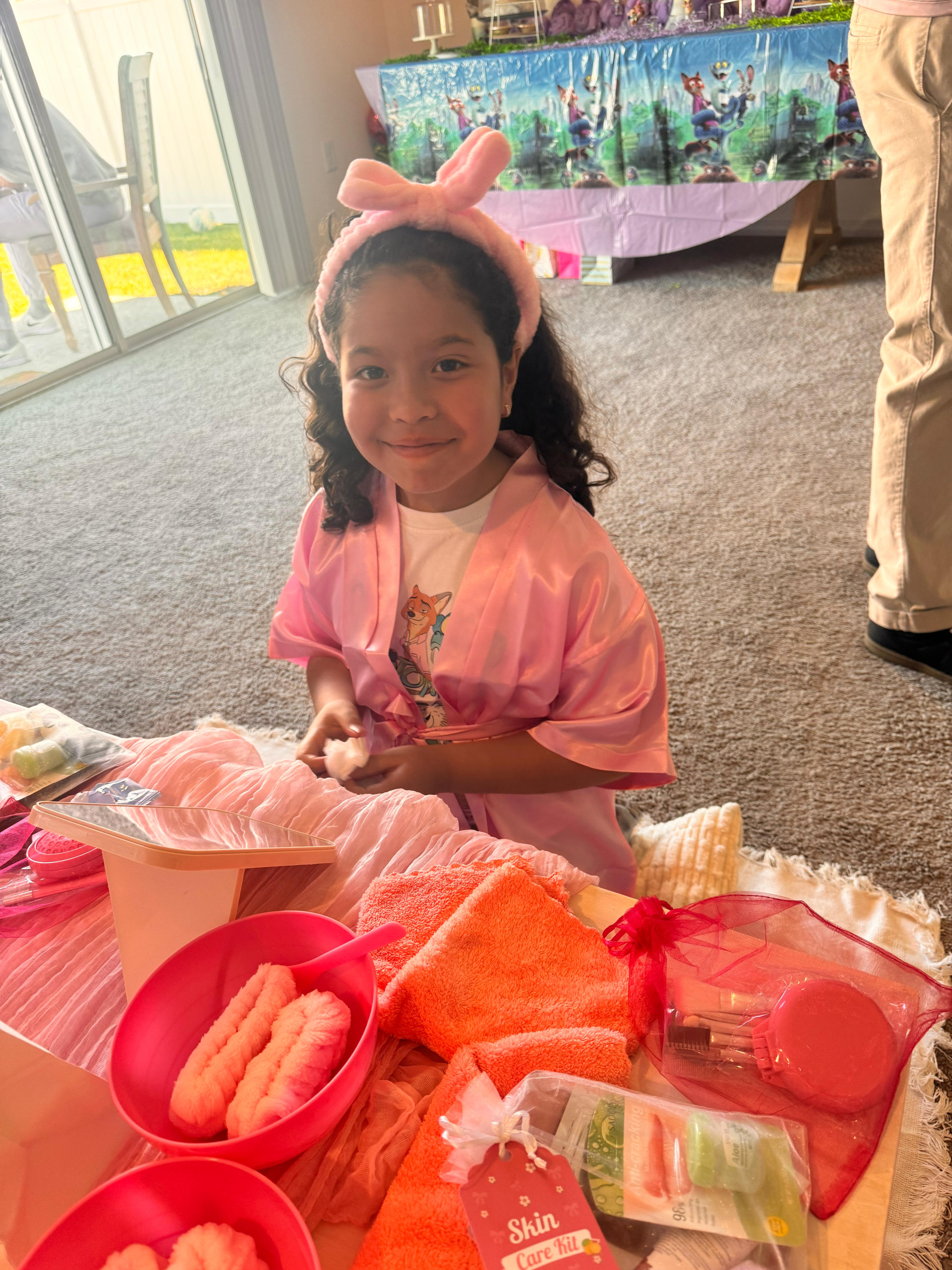 Happy girl in pink spa robe and bunny ear headband smiling at a Sparkle Spa kids birthday party by Titi's Adventure